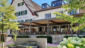 A building with a covered outdoor seating area and a sign reading "Gasthof Kreuz".