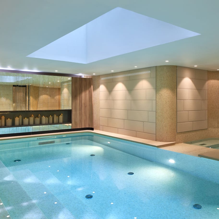 A modern indoor swimming pool with a skylight, tiled walls, and a seating area with candles.