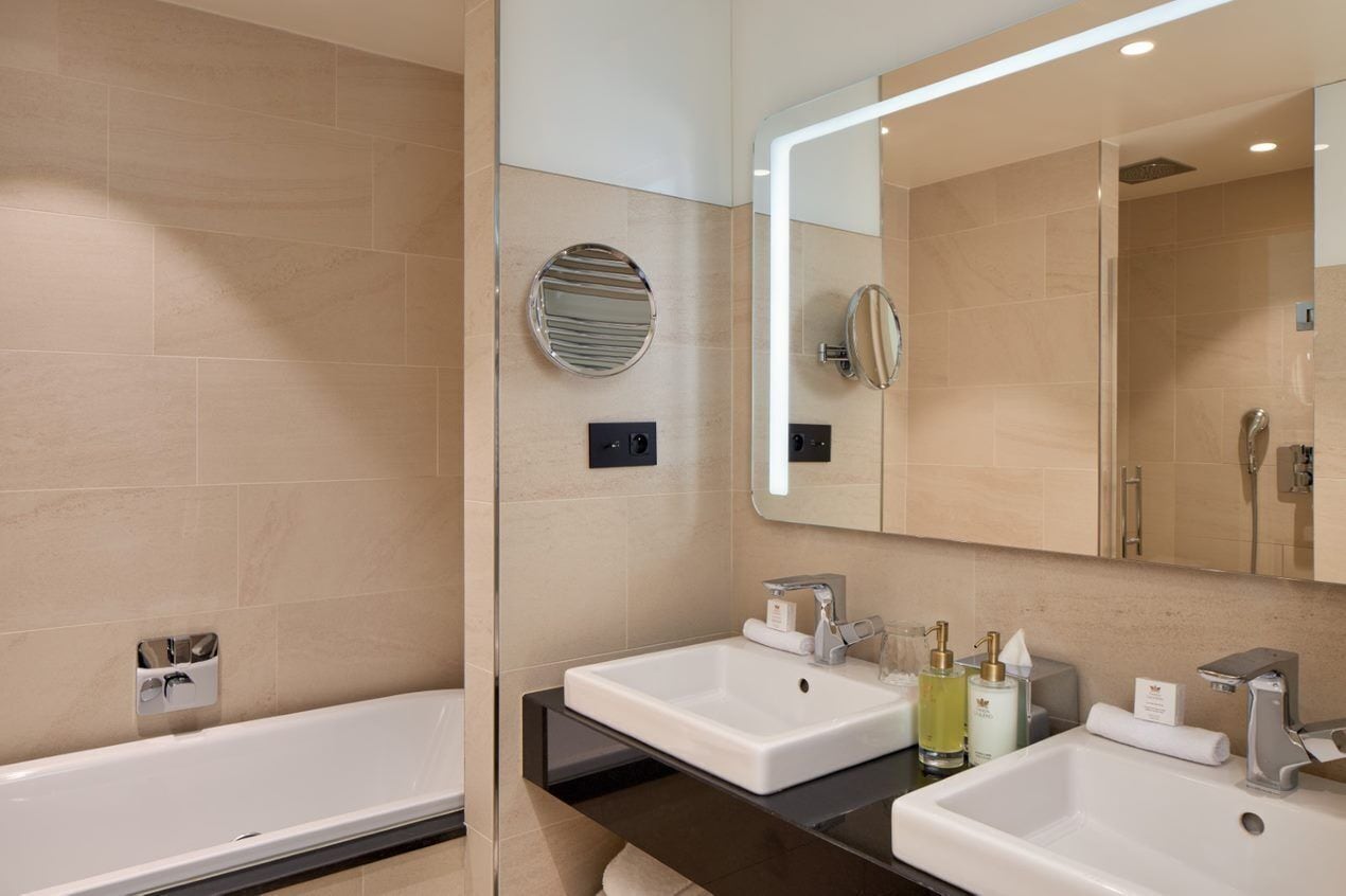 Un baño moderno con bañera, dos lavamanos, un espejo grande y un perchero para toallas.