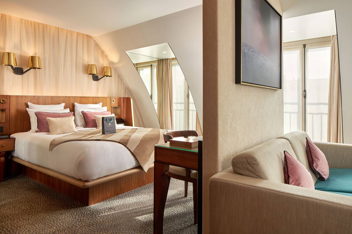 A hotel room with a large bed, a desk, a sofa, and a large window with curtains.