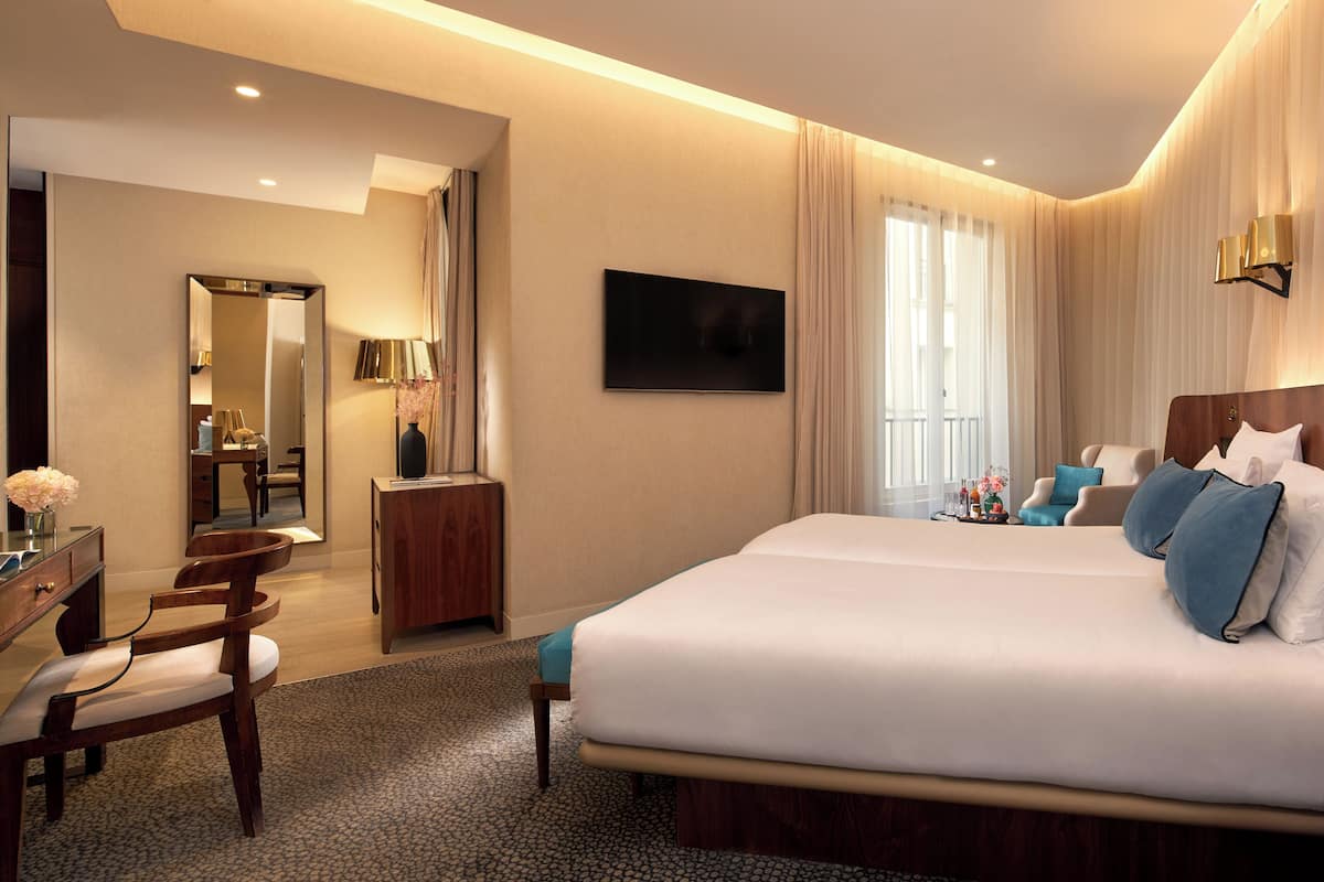 A hotel room with a large bed, a desk, a chair, a mirror, and a TV.