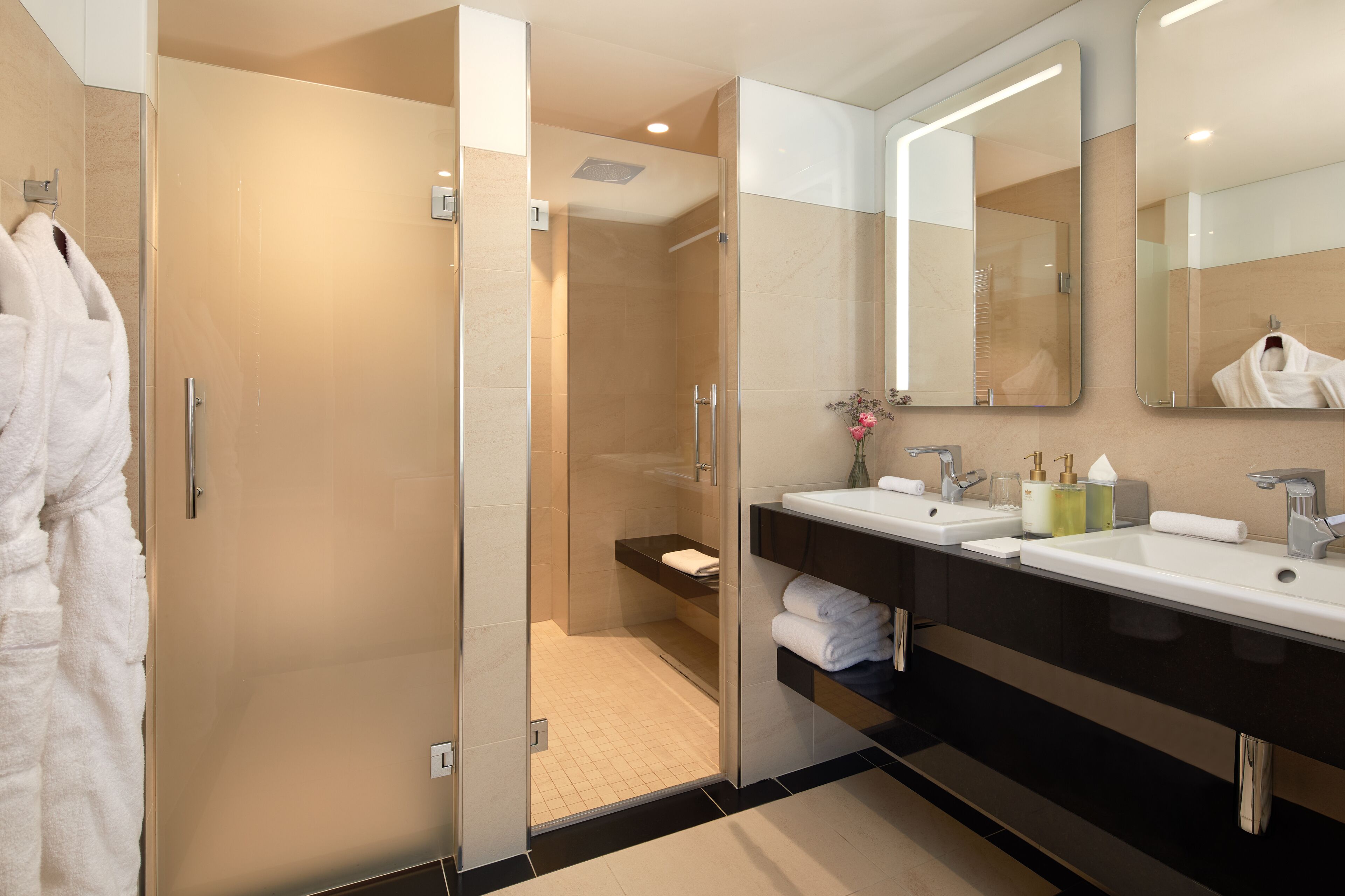 A modern bathroom with a glass-enclosed shower, two sinks, and a large mirror.
