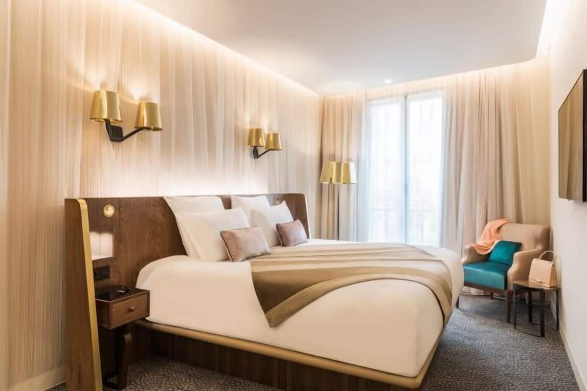 A hotel room with a large bed, bedside lamps, a chair, and a desk.