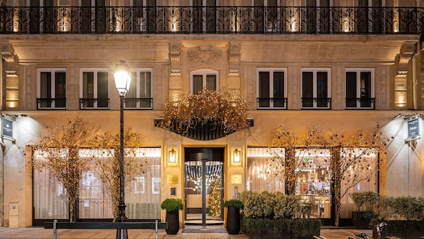 A hotel entrance with a grand facade, a central entrance with a glass door, and a balcony with ornate iron railings.