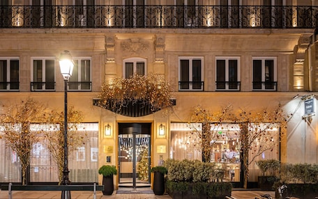A hotel entrance with a grand facade, a central entrance with a glass door, and a balcony with ornate iron railings.