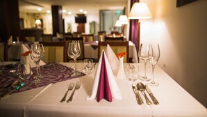 Een hotel eettafel gedekt met een witte tafelkleed, paarse servetten en bestek.