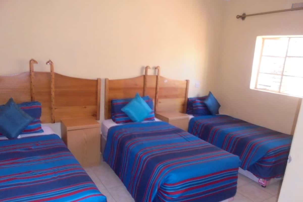 A room with three beds, each with blue and red striped bedding, wooden headboards, and a window providing natural light.
