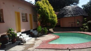 Ein Pool mit roter Umrandung, ein Gebäude mit Reetdach und ein pinkfarbenes Haus mit gelben Türen.