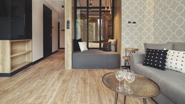 Un salon moderne avec un plancher en bois, un canapé agrémenté de coussins à motifs, une petite table ronde avec des verres et un banc avec des coussins.