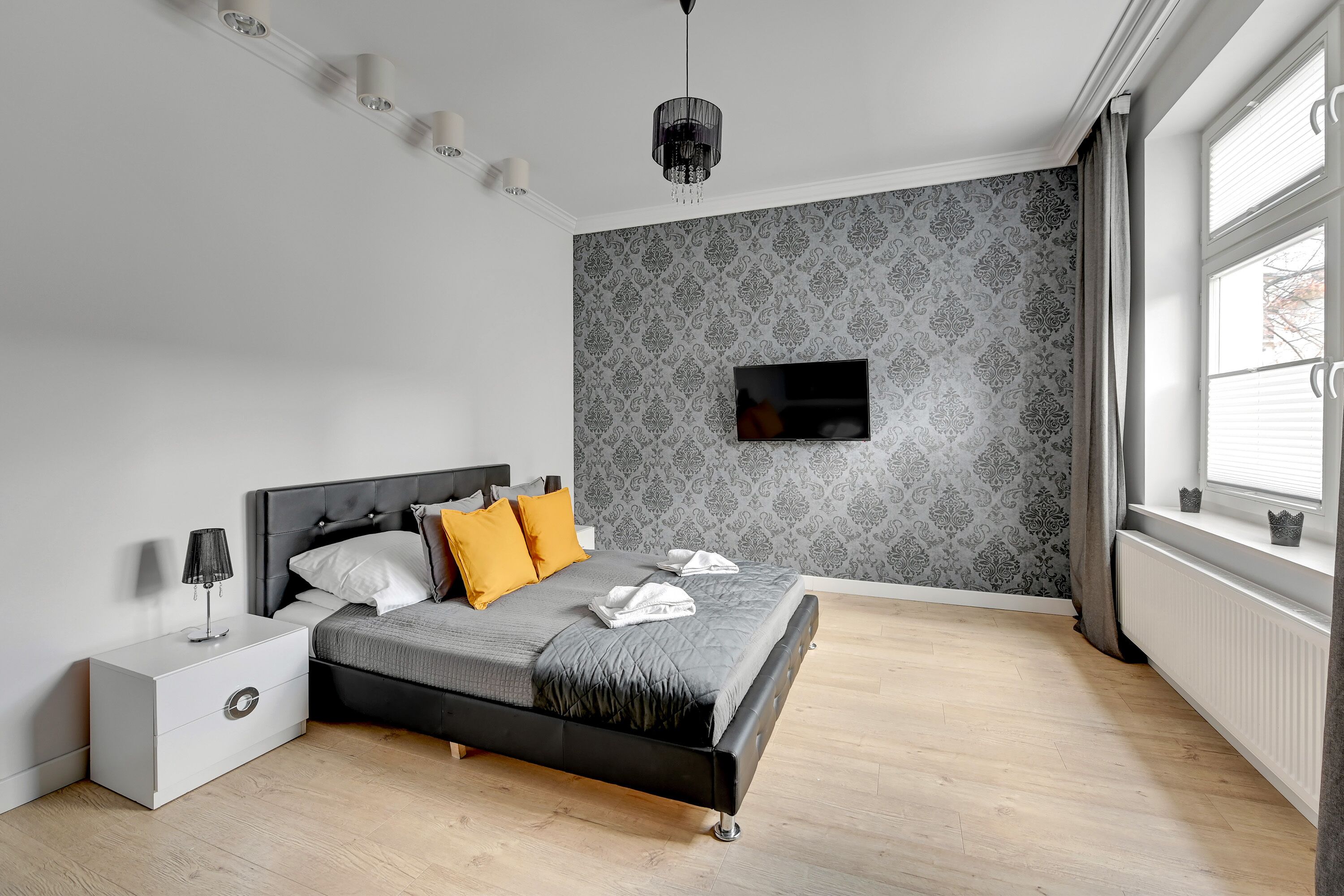 Een slaapkamer met een bed, nachtkastje en een aan de muur bevestigde televisie.
