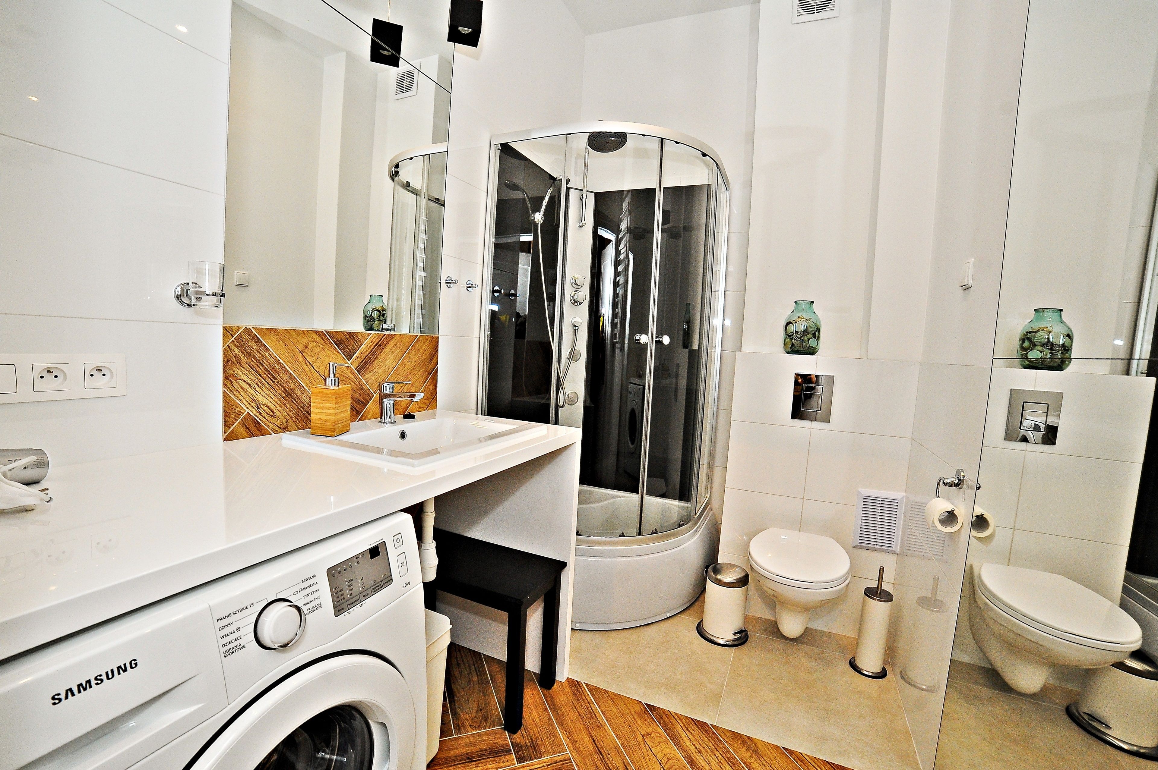 Une salle de bain moderne dotée d’un lave-linge intégré, d’une cabine de douche en verre et d’un espace toilettes séparé.