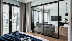 Une chambre moderne avec un grand lit, une porte-fenêtre coulissante donnant sur un balcon et une vue sur la ville.