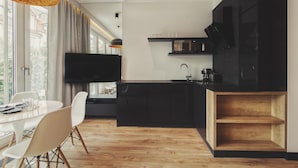 Une cuisine moderne dotée d’un téléviseur à écran plat, de meubles en bois et d’un coin repas avec une table et des chaises blanches.