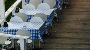 A row of tables with checkered tablecloths and white chairs, arranged on a wooden deck. - Sopocki Zdroj (Sopot)