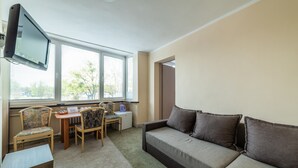 A room with a sofa, two chairs, a small table, a TV, and a window with blinds. - Sopocki Zdroj (Sopot)