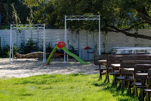 A playground with swings and a slide, surrounded by a white fence and trees.