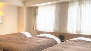 Ett hotellrum med två sängar, var och en med ett mönstrat överkast och kuddar. Det finns ett fönster med gardiner, ett nattduksbord och en vägglampa.