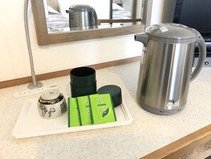 A kitchen counter with a stainless steel kettle, a black container, a white teapot, and three green tea packets.