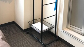 Ett svart metallställ för ytterkläder med en korg som hylla, placerat i ett hotellrum.