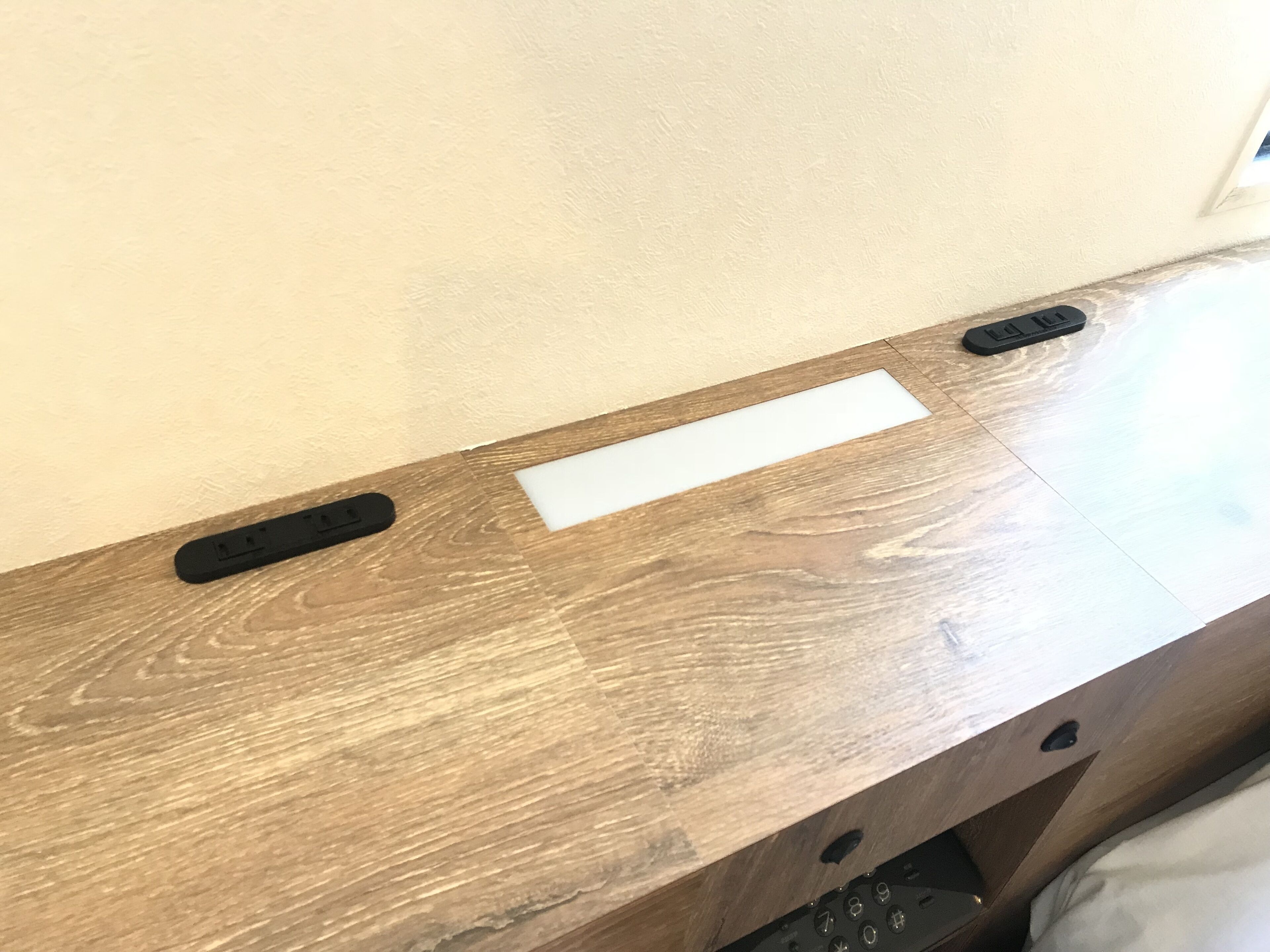 A wooden desk with a white card, two remote controls, and a power outlet.