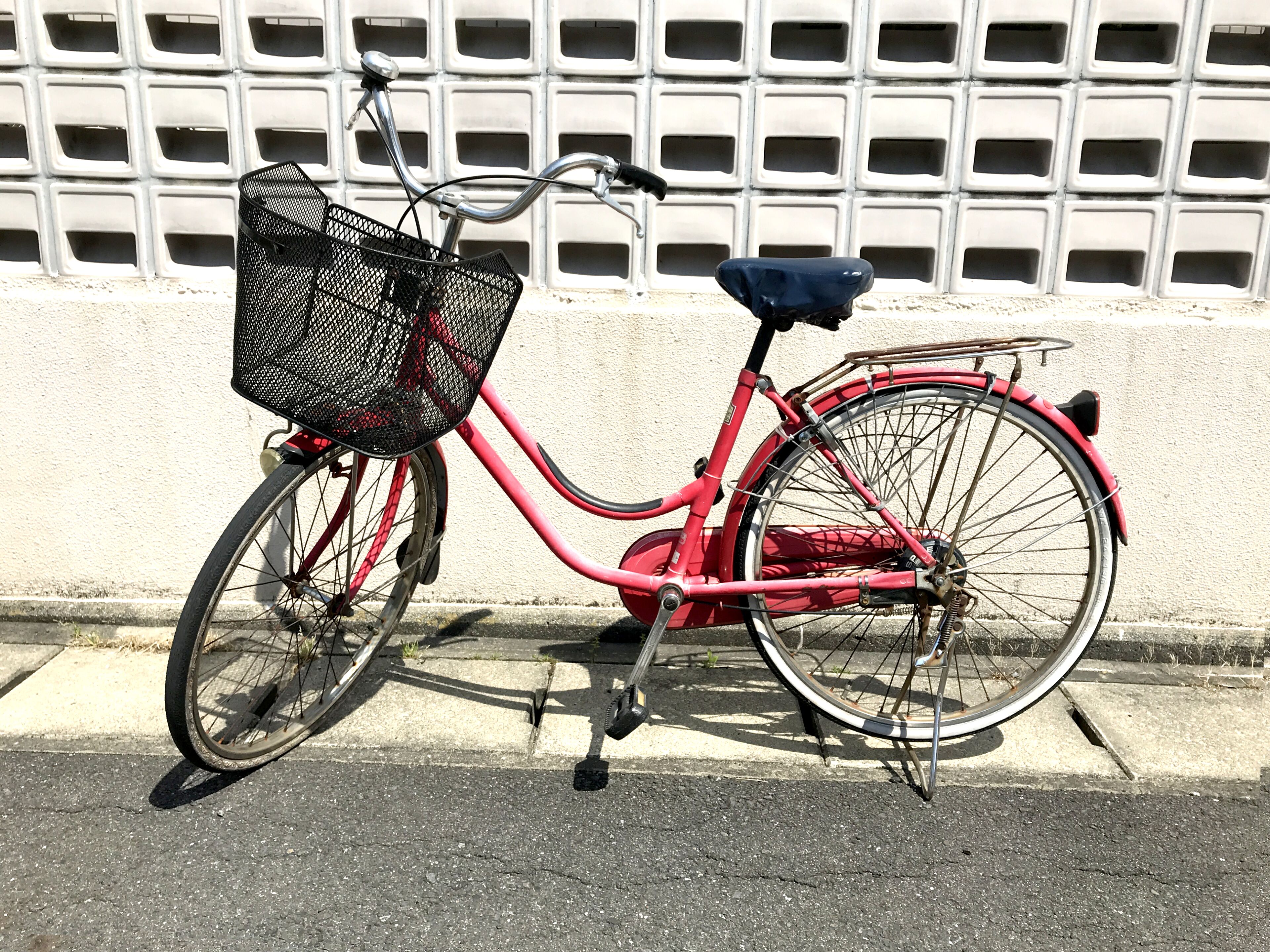 Un vélo rouge avec un panier noir et une selle, garé contre un mur orné d’un motif en forme de grille.