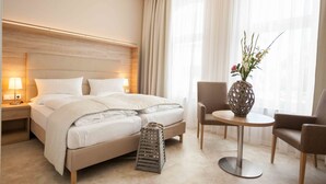 Una habitación de hotel con una cama grande, mesitas de noche, una pequeña mesa redonda con sillas y un jarrón con flores.