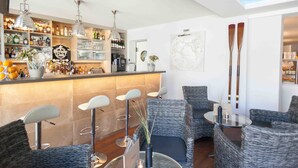Zona de bar con mostrador, estantes llenos de botellas y asientos con sillas de mimbre y una mesa de vidrio.