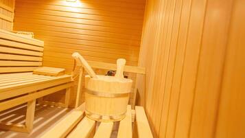 Sauna de fusta amb bancs i un cub d'aigua de fusta amb l'ansa.
