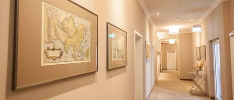 Un pasillo con mapas enmarcados en las paredes, alfombra estampada y una puerta al final.