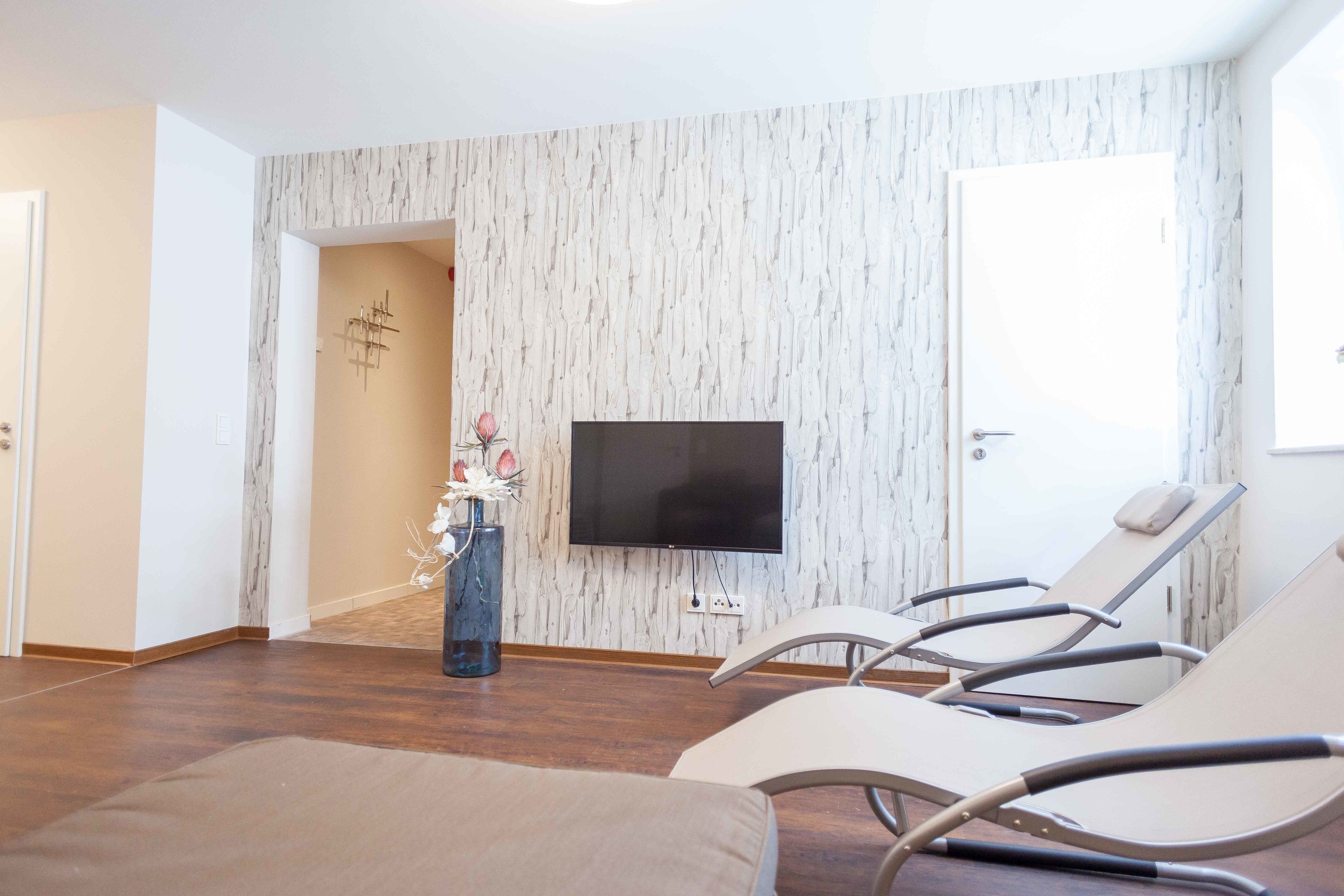 Una habitación moderna con una televisión de pantalla plana montada en una pared texturizada, un ventanal grande y dos sillones reclinables.