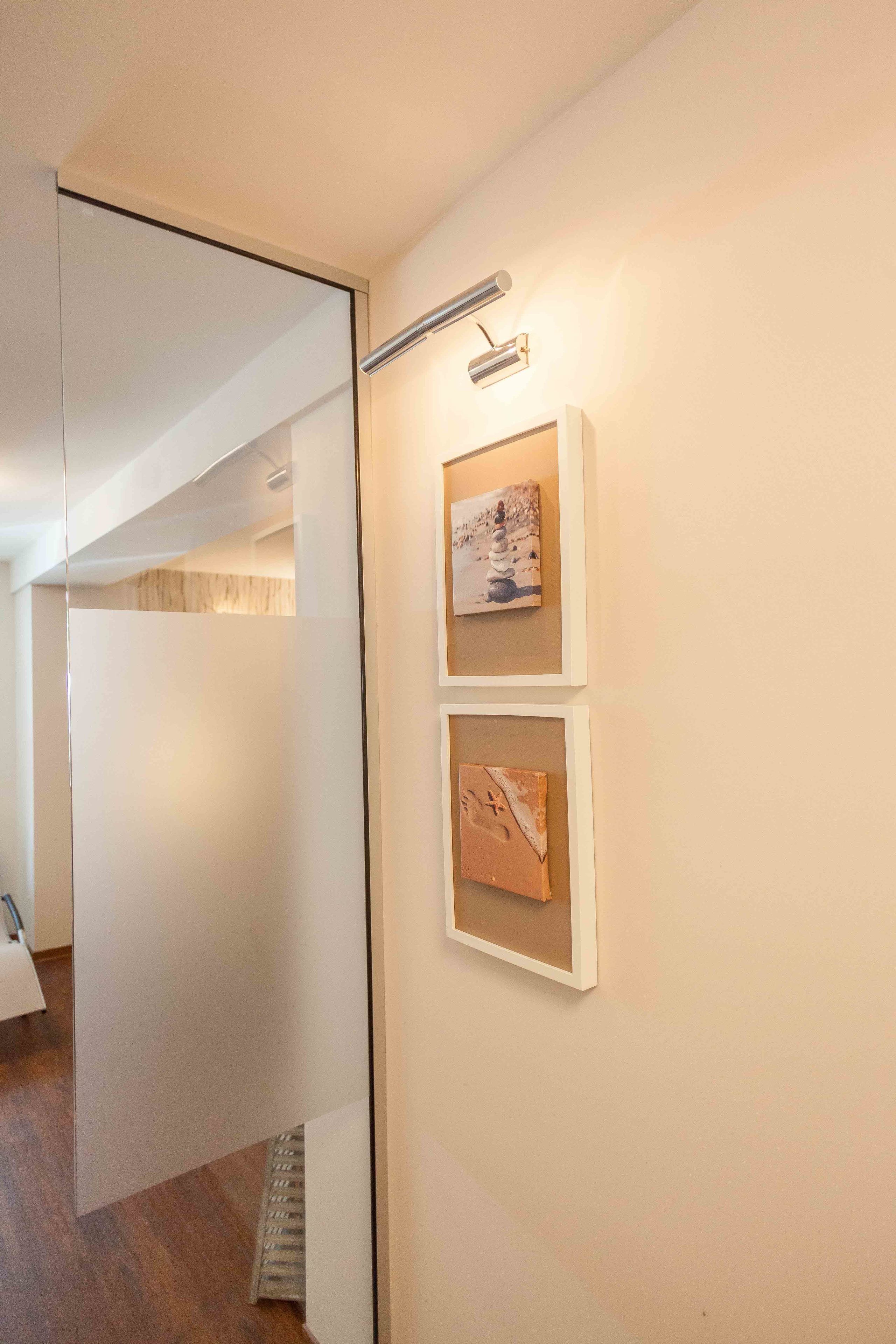 Ein Flur mit Glastrennwand, einem gerahmten Bild an der Wand und einer Deckenleuchte.