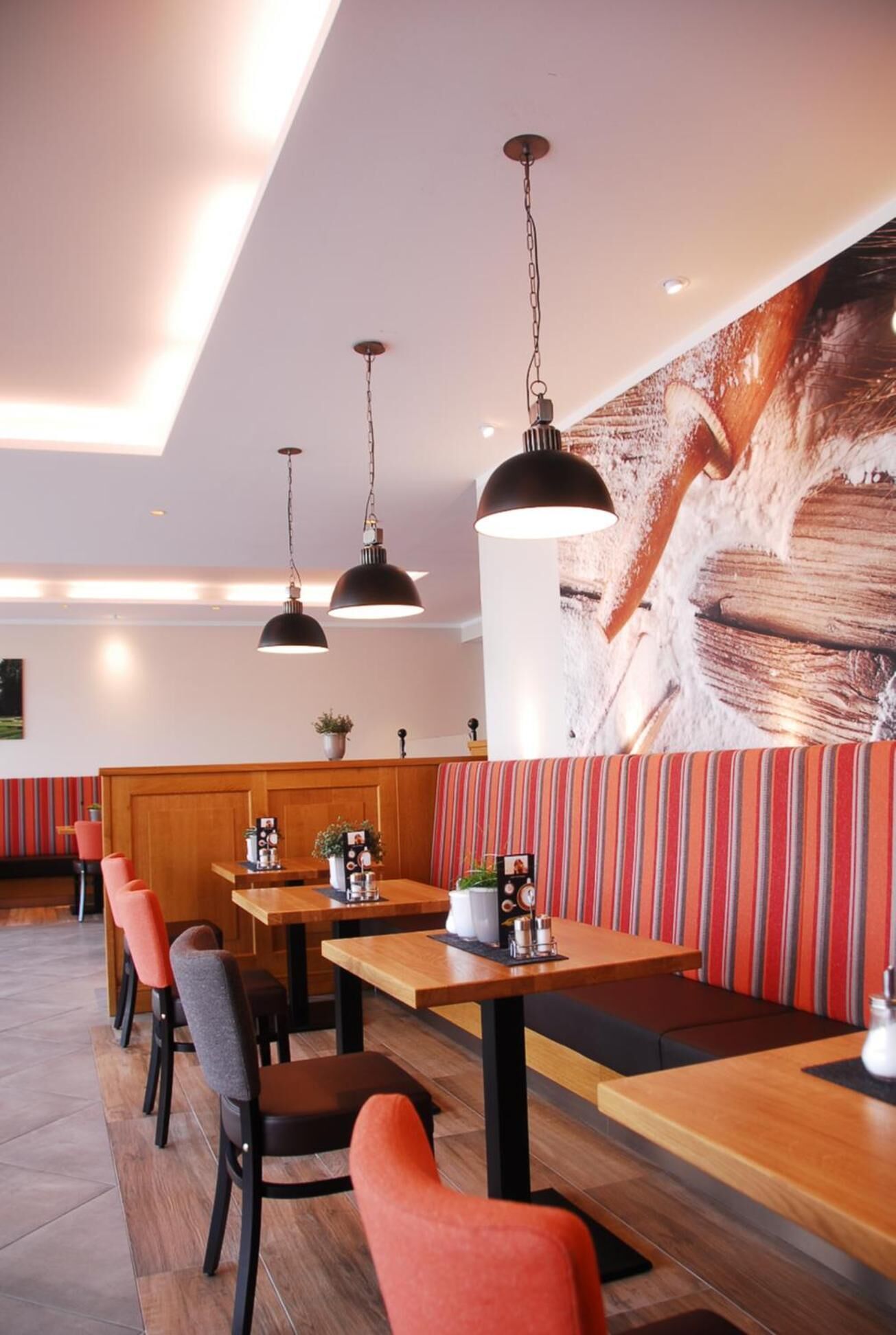 Un restaurant avec des tables et des bancs en bois, des suspensions décoratives et une fresque murale.