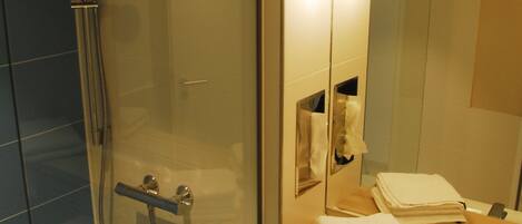 A modern bathroom with a glass-enclosed shower, a sink with a mirror above it, and a towel rack with folded towels.