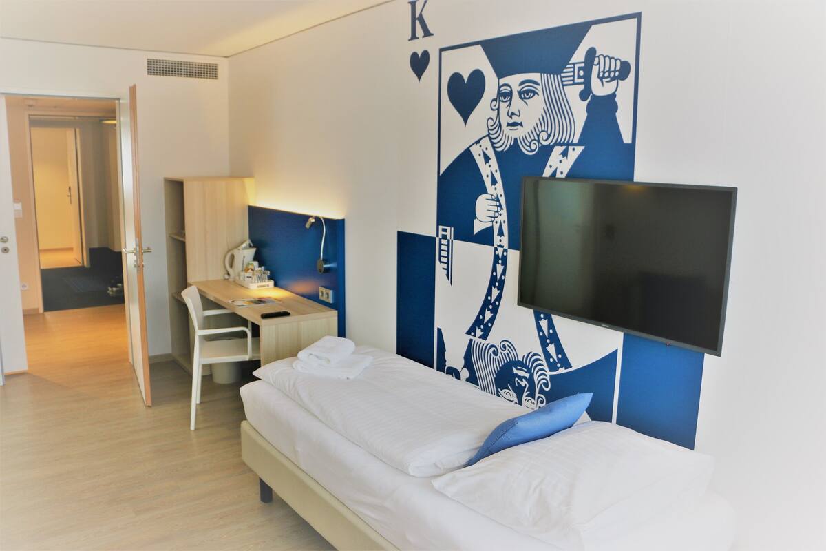 Habitación de hotel con cama, escritorio, silla, televisión de pantalla plana y un mural grande en la pared.