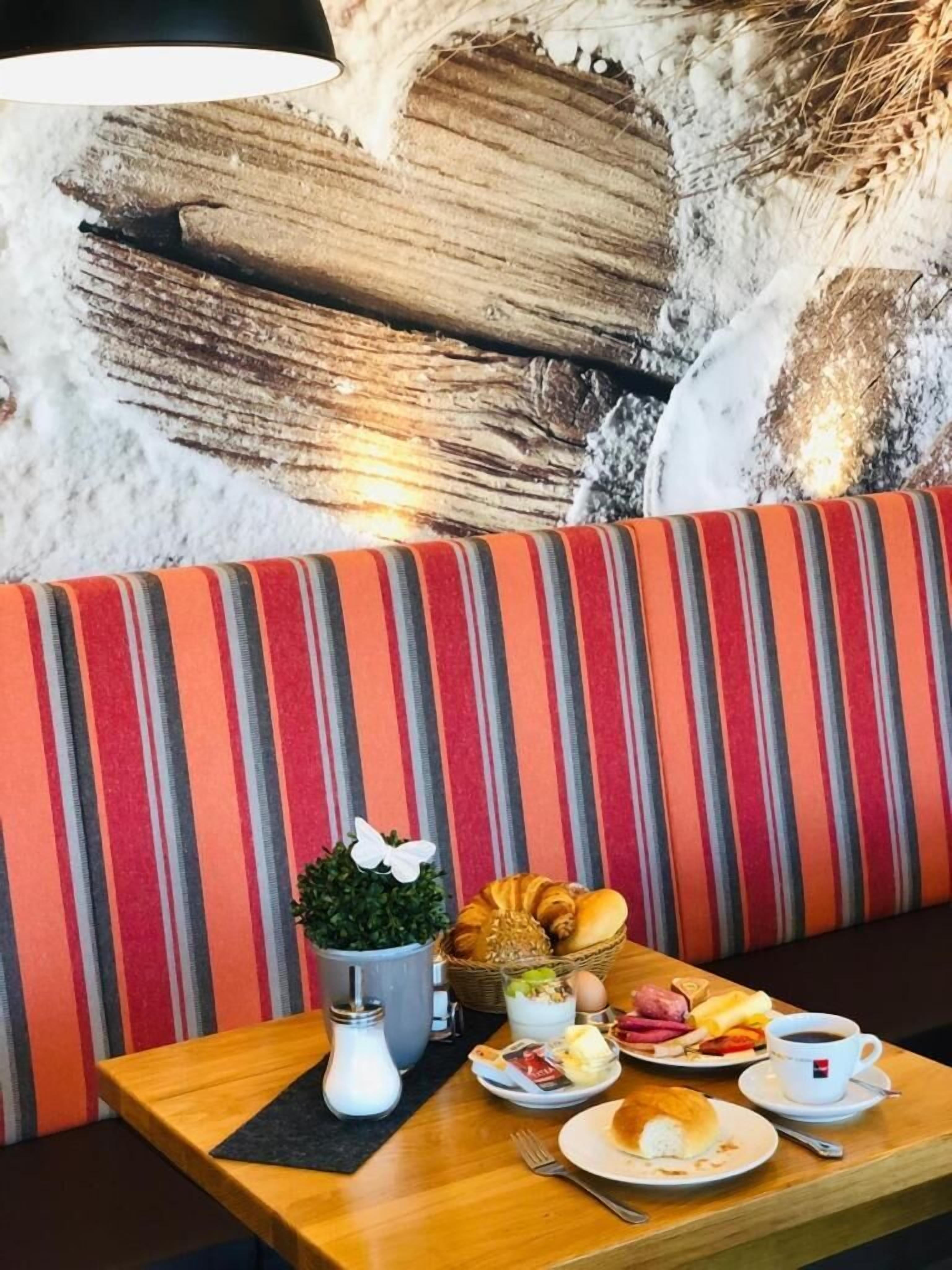 Une table à manger avec des aliments pour le petit-déjeuner, un banc à rayures et un mur au motif texturé.