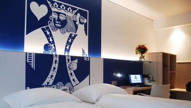 A hotel room with a bed, a desk with a laptop, and a decorative wall piece. - Aparthotel Paderborn (Paderborn)