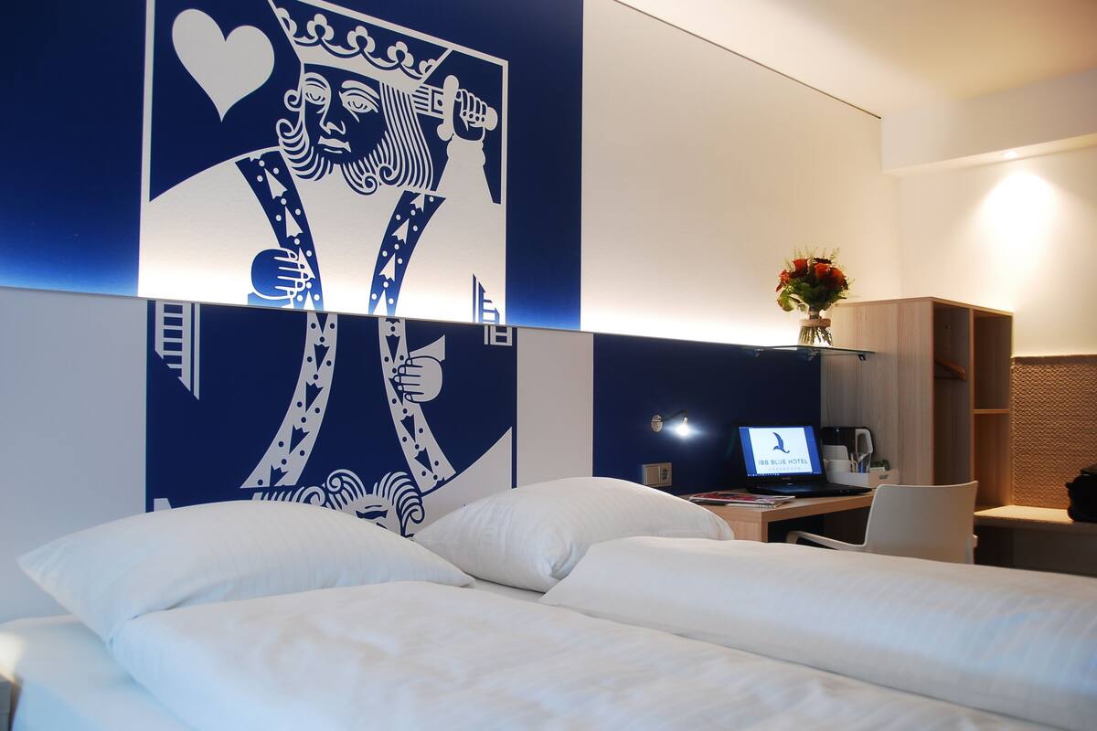 Una habitación de hotel con una cama, un escritorio con una computadora portátil y un adorno en la pared.