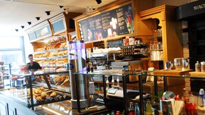 Mostrador de una cafetería con un menú, máquinas de café y una variedad de productos de repostería.