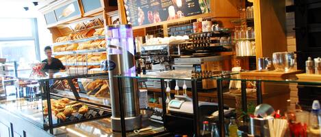 Mostrador de una cafetería con un menú, máquinas de café y una variedad de productos de repostería.