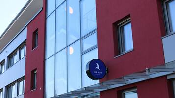 Ein modernes Gebäude mit roter Fassade, großen Fenstern und einem blauen Schild, das ein Hotel anzeigt.