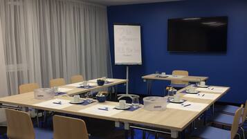 A conference room with a long table, chairs, a whiteboard, and a flat-screen TV.