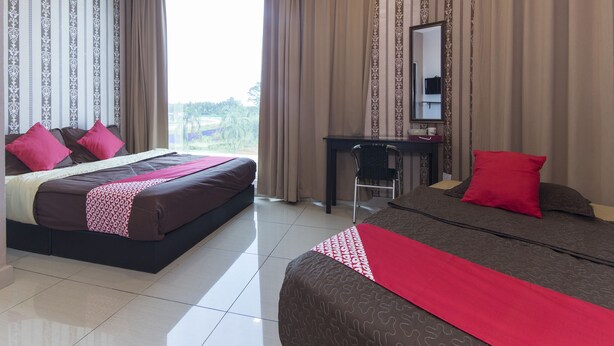 A hotel room with a bed, a desk, and a chair. There is a window with curtains, and a view of the outside. - Night Queen Hotel (Sepang)