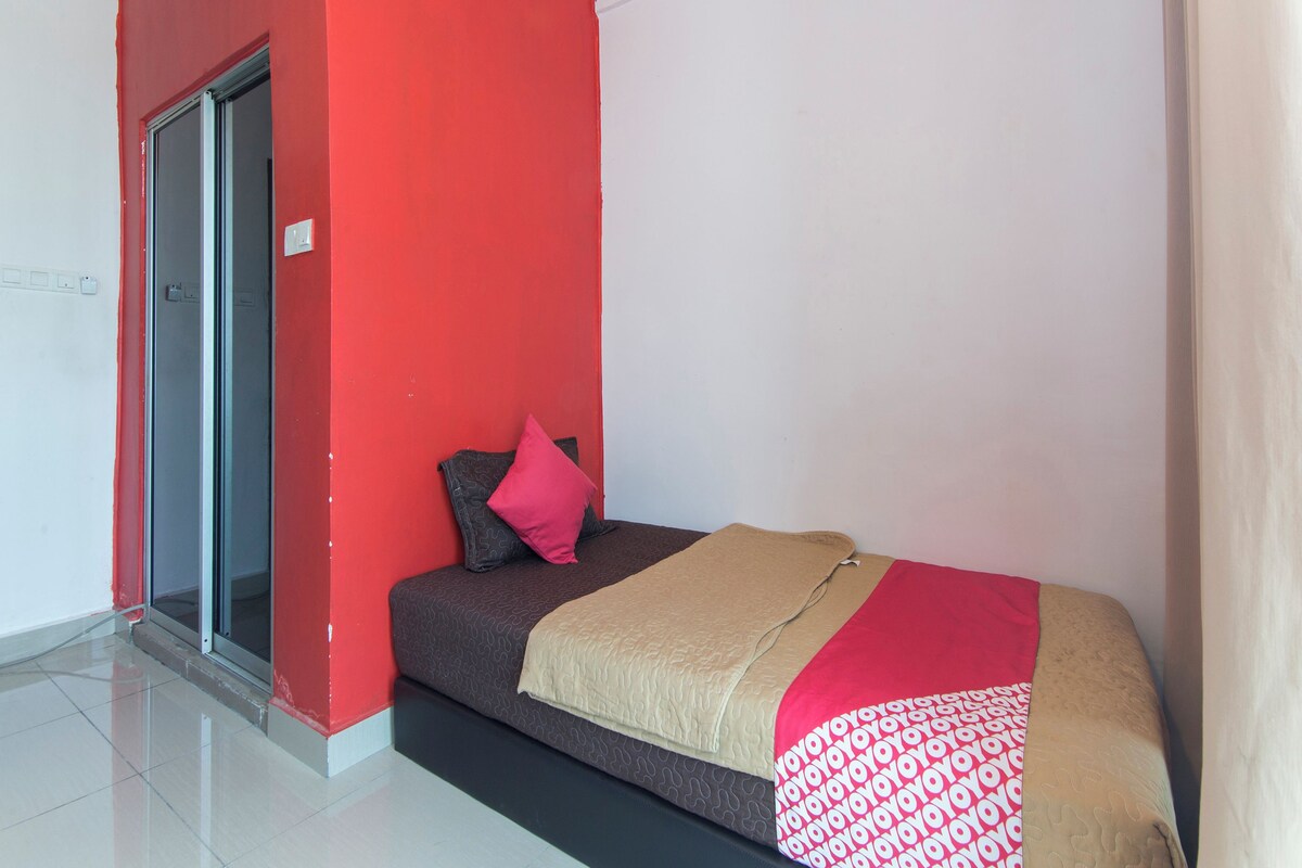 A small, modern bedroom with a red accent wall, a sliding glass door, a bed with a patterned bedspread, and a single pillow.