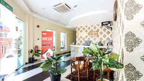 A hotel lobby with a check-in counter, a reception desk, and a seating area with chairs and potted plants. - Night Queen Hotel (Sepang)