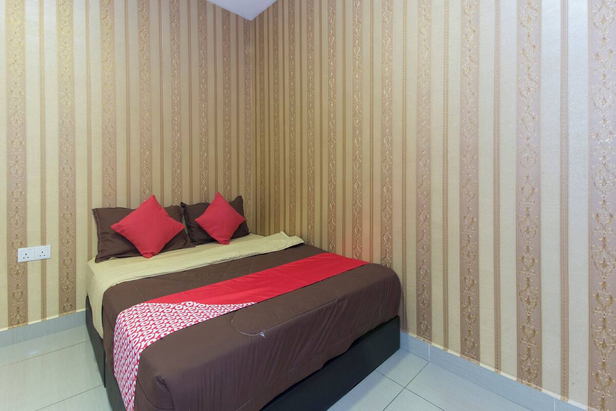A neatly made bed with a brown and red bedspread, a red blanket, and two red pillows. The room has striped wallpaper and a white ceiling.