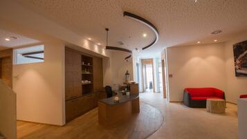 Un intérieur moderne avec un comptoir d’accueil incurvé, des meubles en bois, un canapé rouge et un escalier.