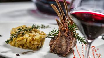 Un plato con un asado de cordero, patatas y una copa de vino tinto.