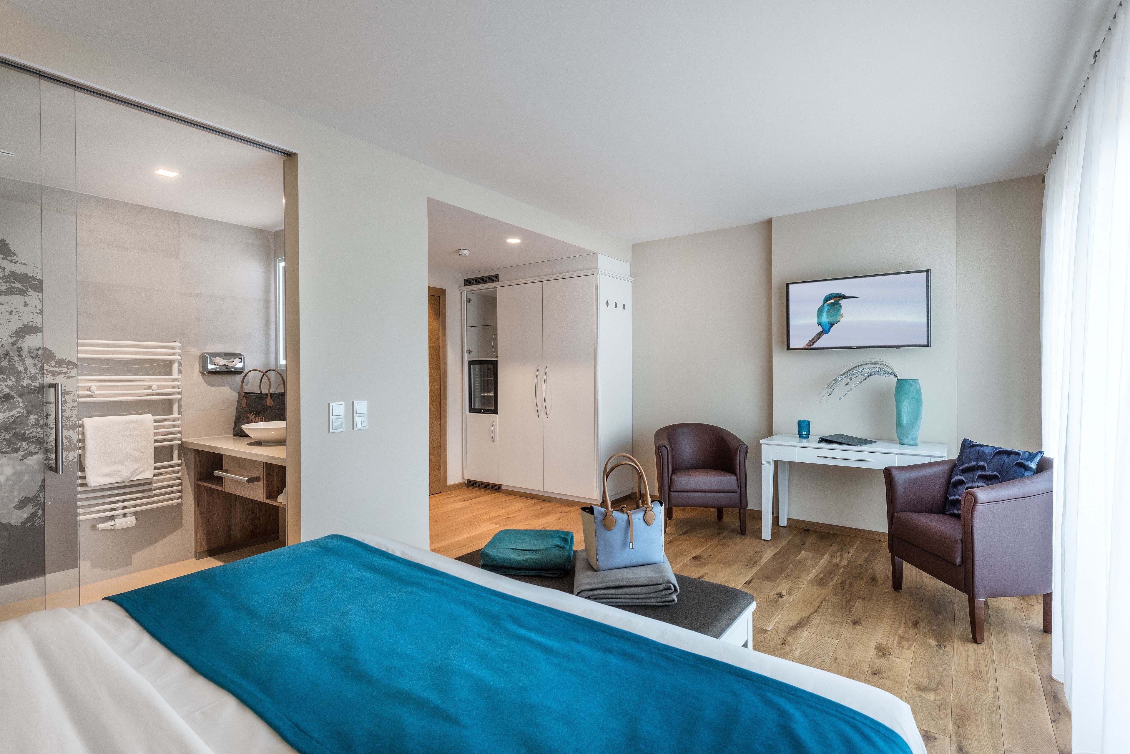 A modern hotel room with a bed, a desk, a chair, and a bathroom.