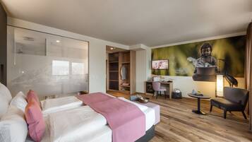 A modern hotel room with a large bed, a desk, a chair, a wardrobe, and a Buddha statue.