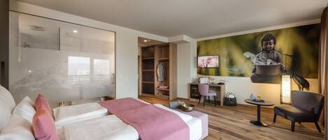 A modern hotel room with a large bed, a desk, a chair, a wardrobe, and a Buddha statue.